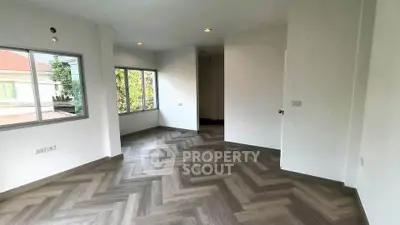 Spacious room with elegant herringbone flooring and large windows offering natural light.