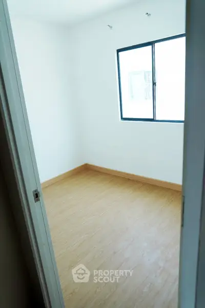 Bright empty room with wooden flooring and large window, perfect for customization.