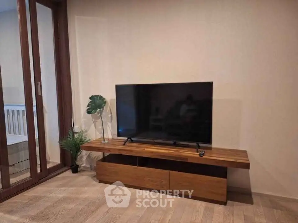 Modern living room with sleek TV stand and large flat-screen TV, adjacent to a balcony with wooden flooring.