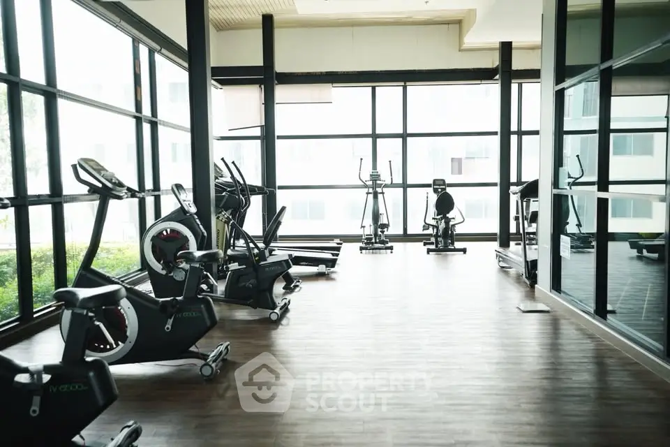 Spacious gym with modern exercise equipment and large windows for natural light.