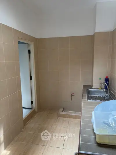 Spacious utility room with tiled walls and sink, ideal for laundry or storage.