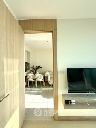 Modern living room with TV and open view to dining area, featuring sleek wooden finishes.