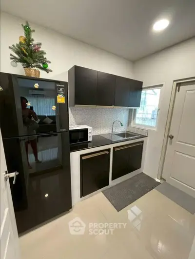 Modern kitchen with sleek black cabinets and appliances, featuring a compact layout and stylish decor.