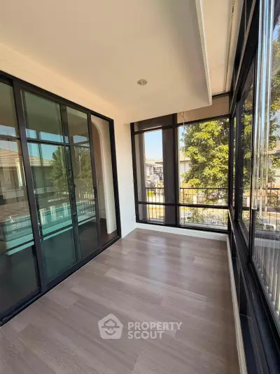 Spacious sunlit balcony with large glass doors and scenic view, perfect for relaxation.