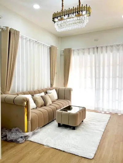 Elegant living room with plush beige sofa, chic chandelier, and natural light through sheer curtains.