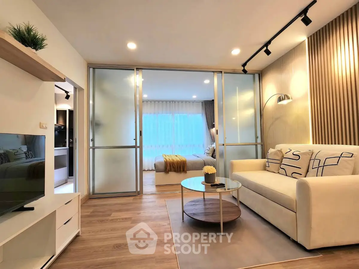 Modern living room with cozy sofa and stylish decor leading to a bright bedroom through sliding glass doors.