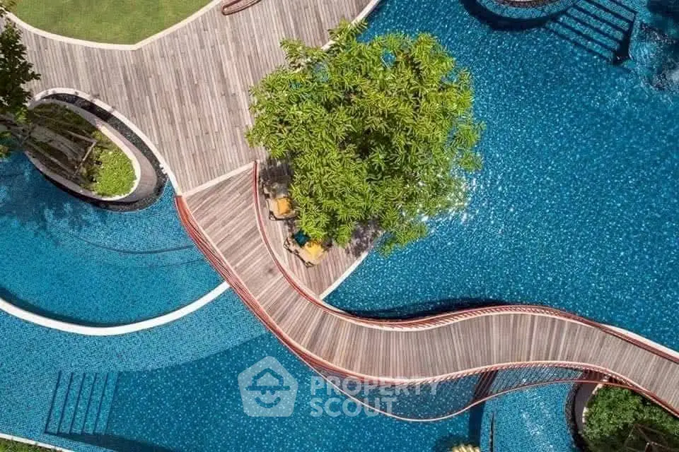 Stunning aerial view of luxurious pool with wooden bridge and lush greenery.