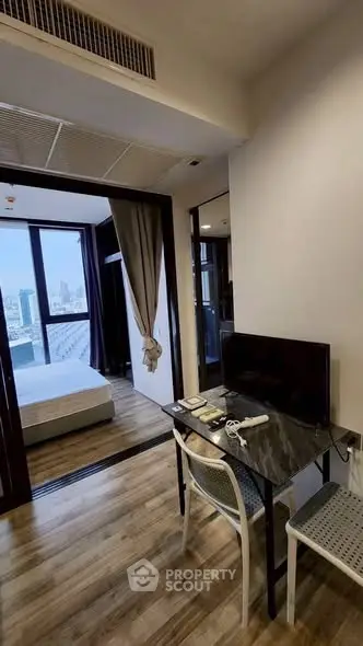 Modern apartment interior with bedroom view and workspace setup, featuring sleek design and cityscape backdrop.