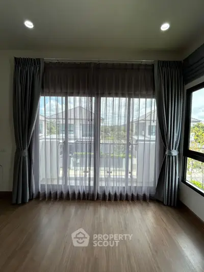 Spacious room with large window and elegant curtains offering natural light and outdoor view.