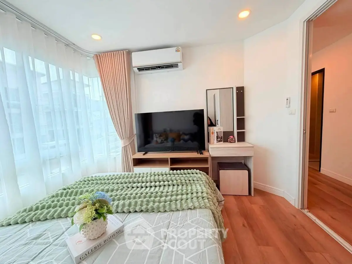 Modern bedroom with large window, stylish decor, and flat-screen TV in a cozy apartment.