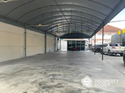 Spacious covered parking area with multiple vehicles and a small office building in the background.