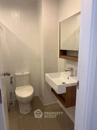 Modern bathroom with sleek fixtures and neutral tiles, featuring a compact design.
