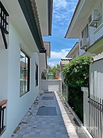 Charming residential alleyway with lush greenery and modern architecture under a clear blue sky.