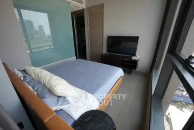 Modern bedroom with large window and city view, featuring a sleek TV setup and stylish decor.
