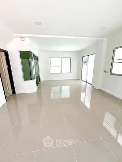 Spacious empty living room with large windows and glossy tiled floor in modern home.