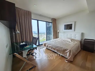 Spacious bedroom with large window and city view, featuring modern furniture and wooden flooring.