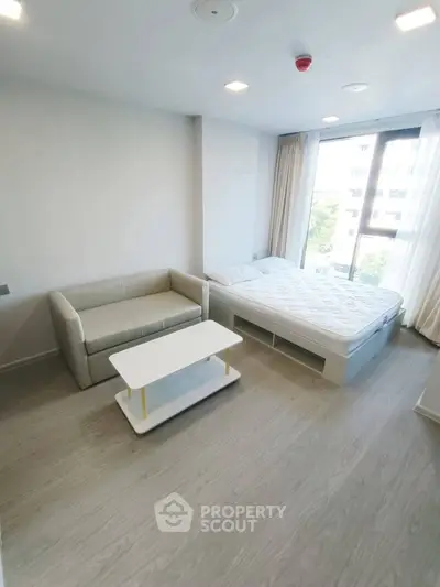Modern studio apartment with cozy bed and stylish sofa in bright, airy space.