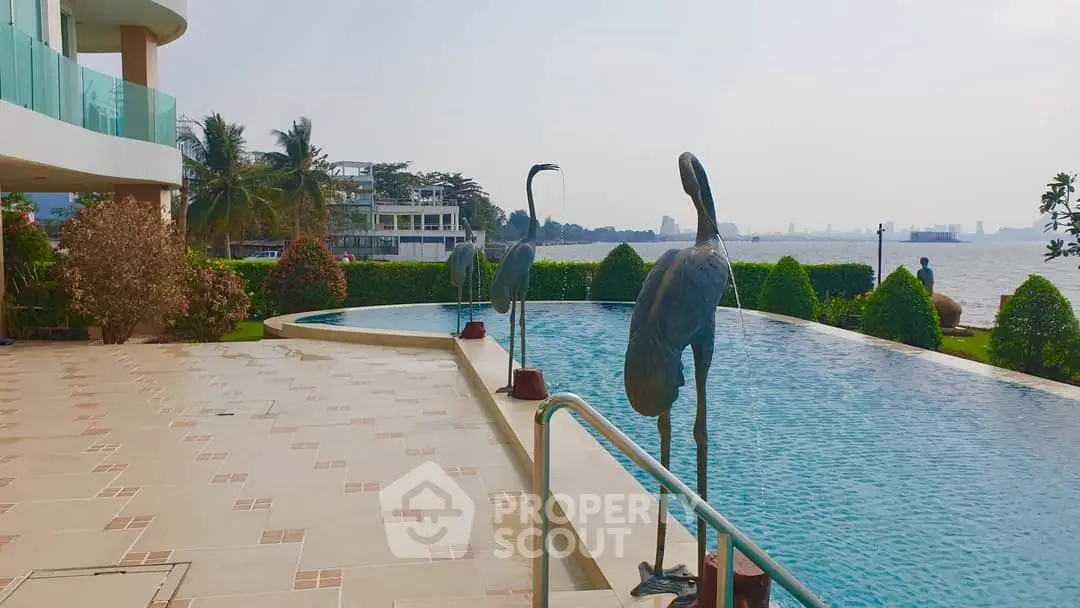 Luxurious waterfront pool area with elegant sculptures and lush greenery, offering serene views and modern amenities.