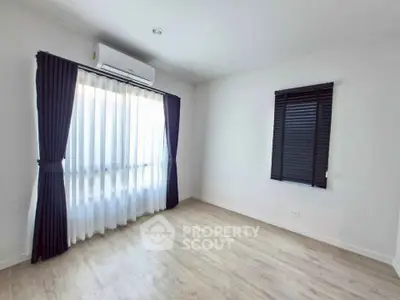 Spacious empty room with wooden flooring and large window, perfect for customization.