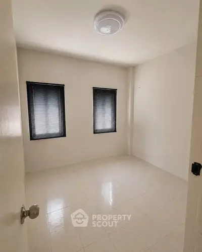 Spacious empty room with tiled floor and two windows, perfect for customization.