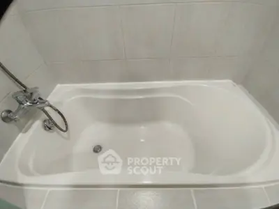Modern bathroom with sleek white bathtub and tiled walls.
