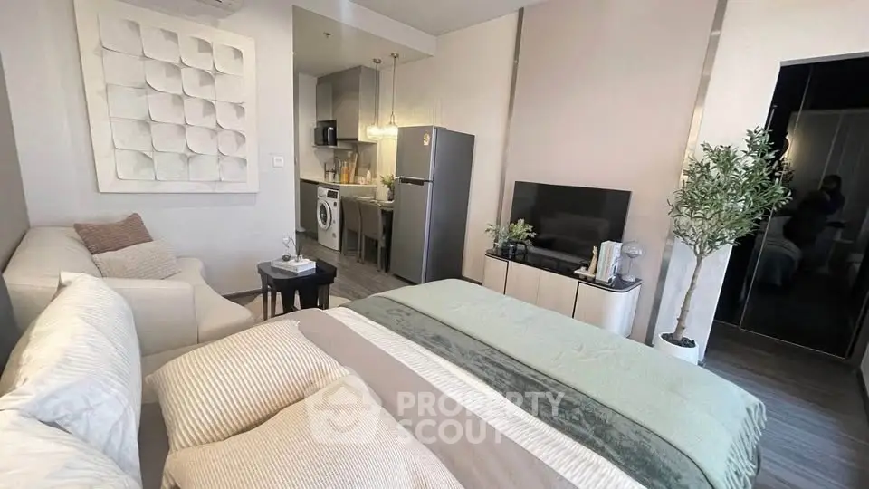 Modern studio apartment with cozy living area and compact kitchen featuring washing machine and fridge.