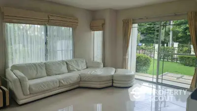 Spacious living room with large windows and garden view, featuring a modern white sectional sofa.