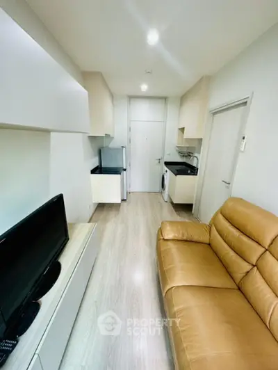 Cozy modern studio apartment with sleek white cabinetry, integrated appliances, and a comfortable leather sofa, perfect for urban living.