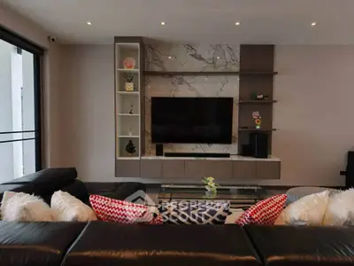 Modern living room with stylish decor and large TV, featuring a sleek leather sofa and decorative shelving.