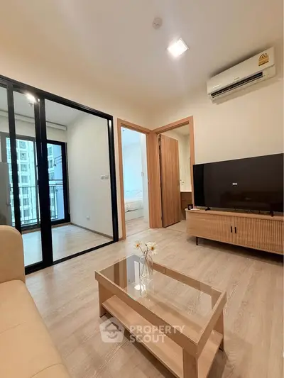 Modern living room with sleek furniture and large TV, featuring a view into a cozy bedroom.