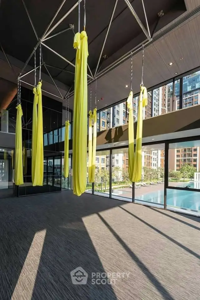 Modern gym with aerial yoga setup and pool view in luxury apartment complex.