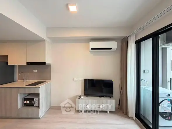 Modern living room with open kitchen and balcony view, featuring sleek appliances and stylish decor.