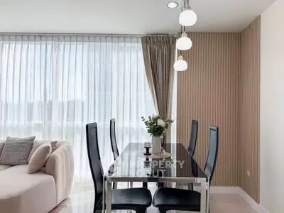 Modern dining area with elegant black table and chairs, adjacent to a cozy living room with natural light.