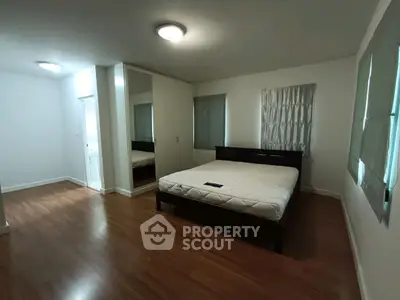 Spacious bedroom with wooden flooring and large windows for natural light.