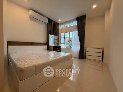 Spacious bedroom with large window and modern furnishings in a bright, airy apartment.