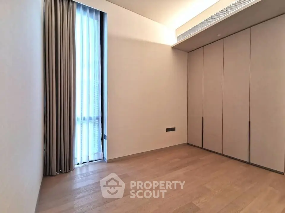 Spacious empty room with wooden flooring and large window, perfect for customization.