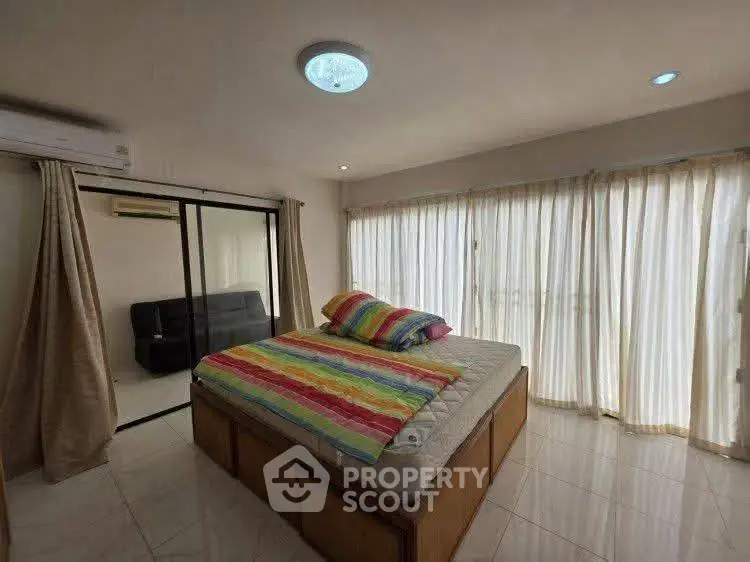 Spacious bedroom with large windows and colorful bedding in a modern apartment.