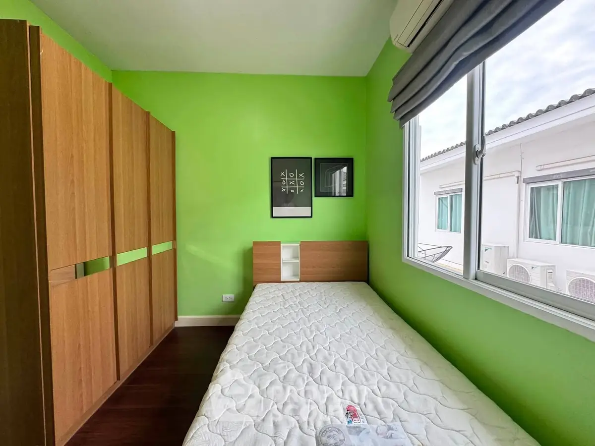 Bright bedroom with green walls, large window, and wooden wardrobe, perfect for a cozy living space.
