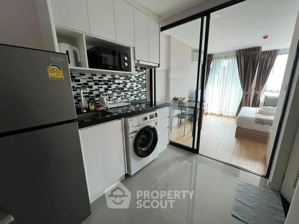 Modern compact kitchen with washing machine and view into cozy bedroom