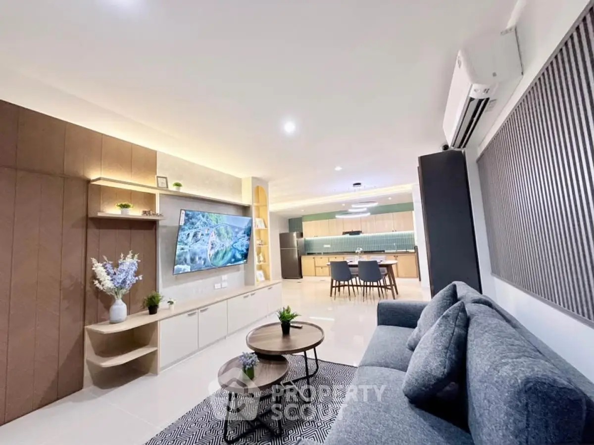 Modern living room with stylish decor and open kitchen layout, featuring sleek furniture and ambient lighting.