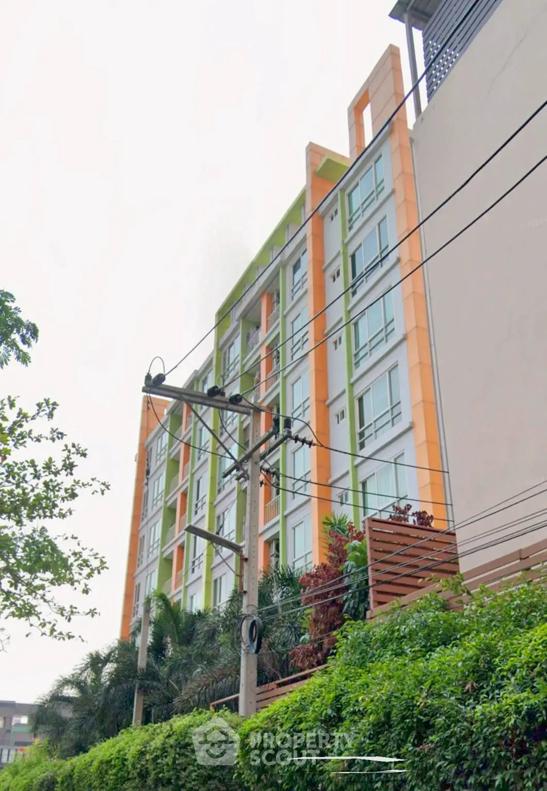 Modern urban apartment building with vibrant orange accents and lush greenery.