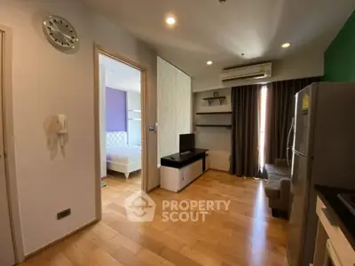 Modern apartment interior with wooden flooring, open living area, and visible bedroom.