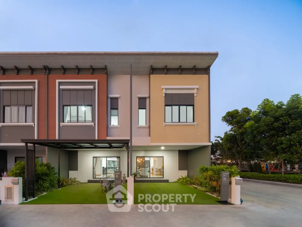 Elegant two-story townhouse with a modern facade, featuring a covered parking space and a well-manicured front lawn, captured at dusk.
