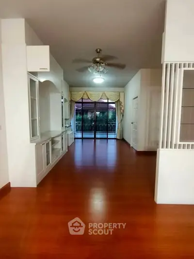 Spacious living room with wooden flooring and large windows leading to balcony.