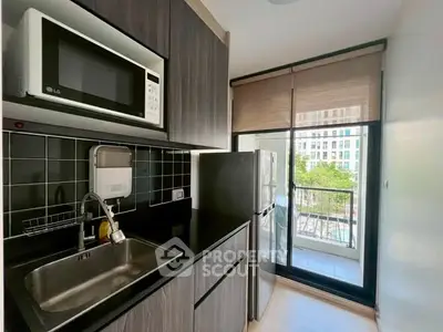 Modern kitchen with sleek cabinetry, microwave, and balcony view in urban apartment.