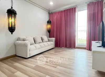 Elegant living room with stylish lanterns and pink curtains, featuring a cozy white sofa and modern TV setup.