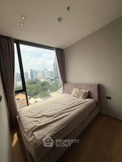 Cozy bedroom with stunning city view and large window, perfect for urban living.