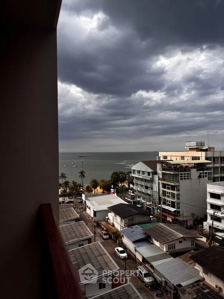 Stunning ocean view from high-rise balcony overlooking cityscape and coastline under dramatic cloudy sky.