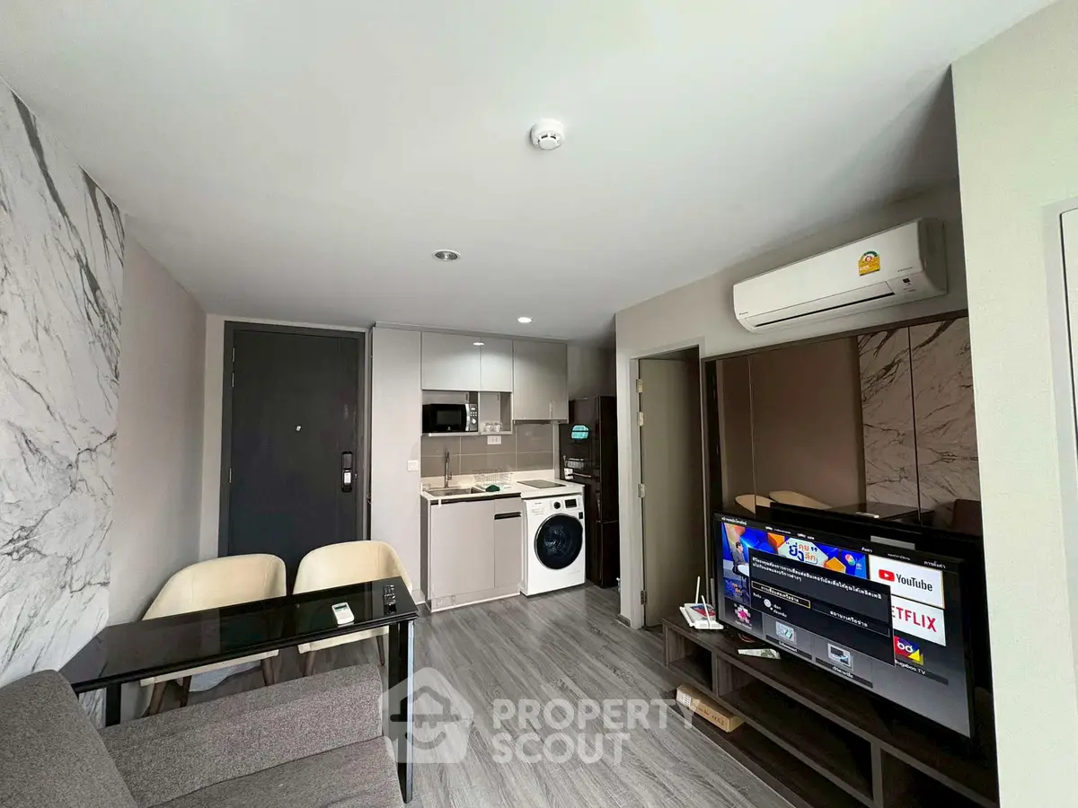 Modern living room with open kitchen and washing machine, featuring sleek design and contemporary furniture.
