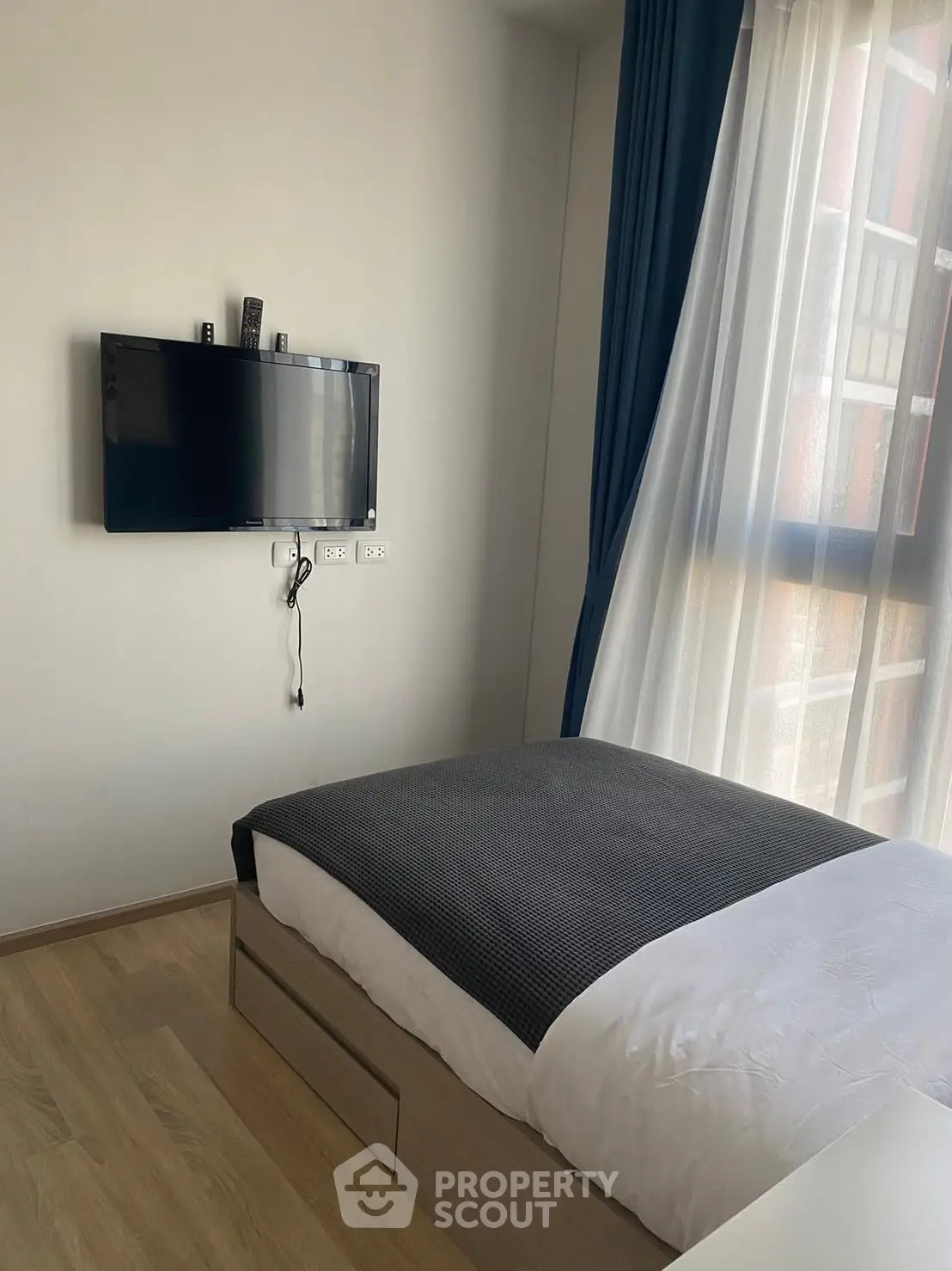 Modern bedroom with wall-mounted TV and large window with blue curtains.